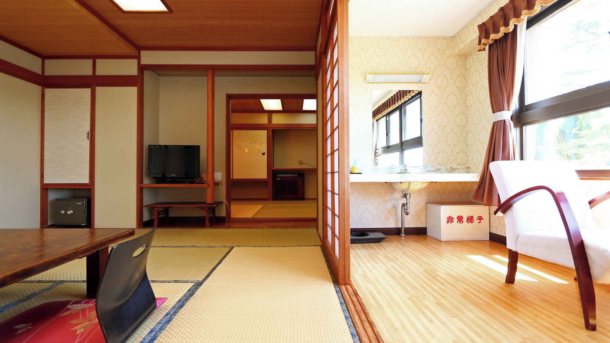 Una habitación japonesa tradicional con suelo de tatami, televisión, caja fuerte y una puerta corredera que da a otra habitación.