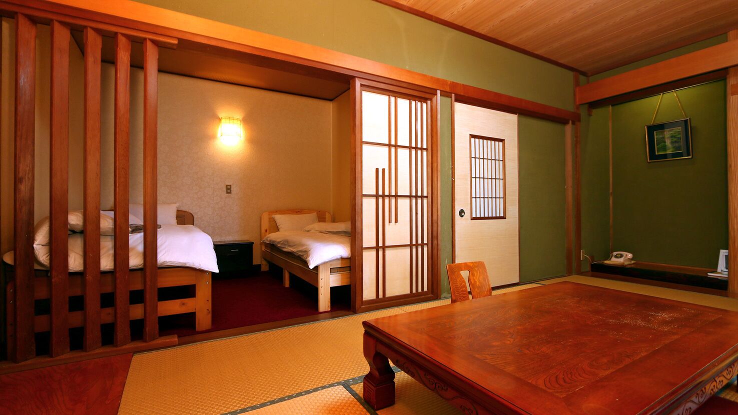 Una habitación japonesa tradicional con suelo de tatami, una mesa de madera, una cama con futón, puertas correderas y un cuadro colgado en la pared.