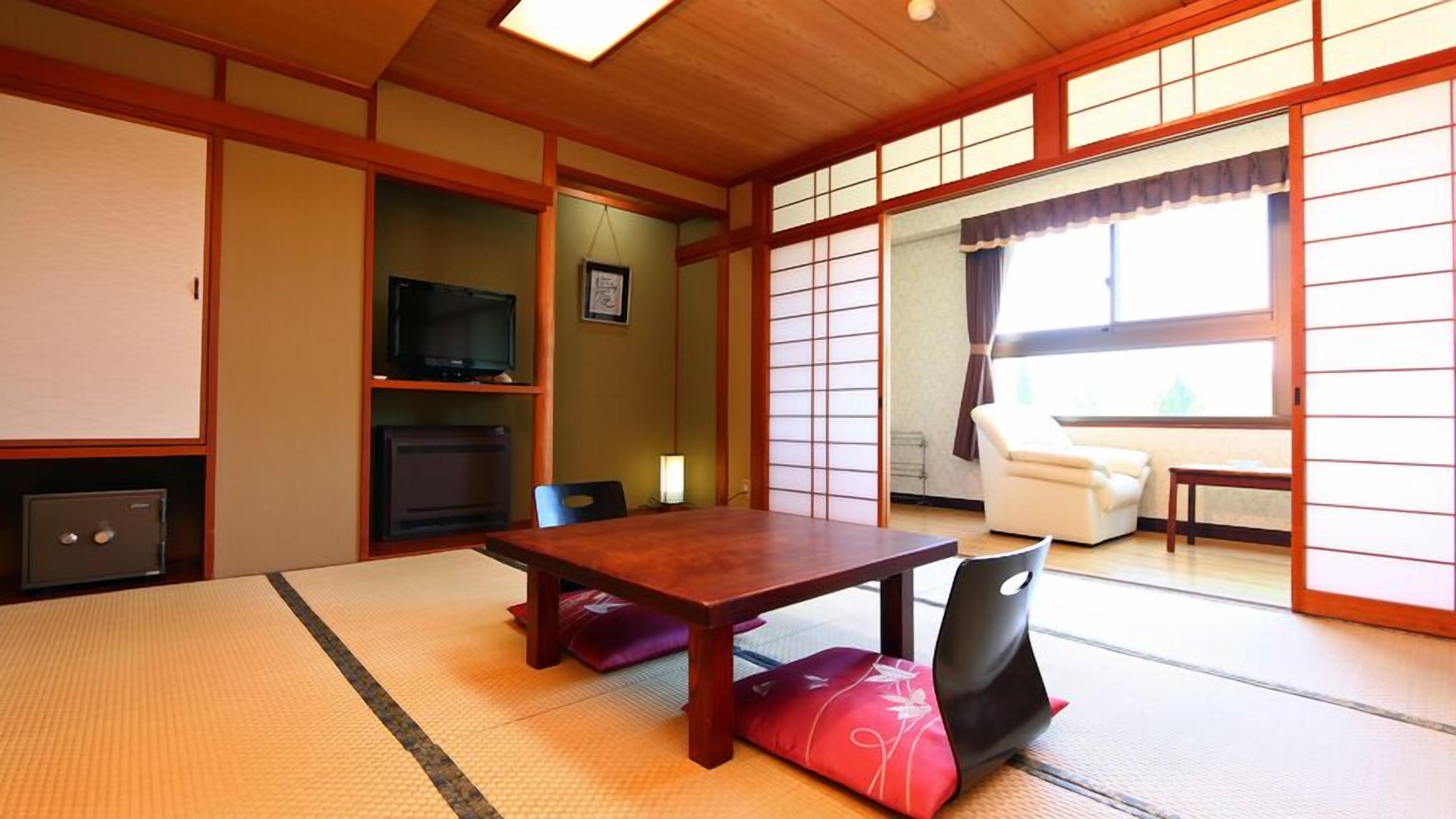 Una habitación japonesa tradicional con suelo de tatami, una mesa baja, un televisor y puertas correderas.