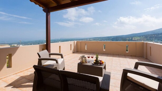 Eine Terrasse mit Korbmöbeln, einem Tisch mit Obst und Getränken sowie einem schönen Blick auf Berg und Meer.