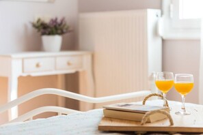 A white chair, a wooden table with a book and two glasses of orange juice, and a white dresser with a plant in the background.