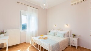 Ein Schlafzimmer mit einem Bett, Nachttischen, einem Schreibtisch, einem Fenster mit Vorhängen und einer Klimaanlage.
