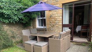 Een terras buiten met rieten meubilair, een tafel en een paarse parasol.