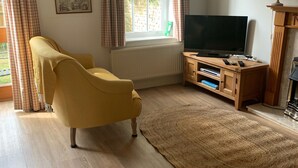 Een woonkamer met een gele fauteuil, een rode bank, een televisie op een houten standaard en een open haard.