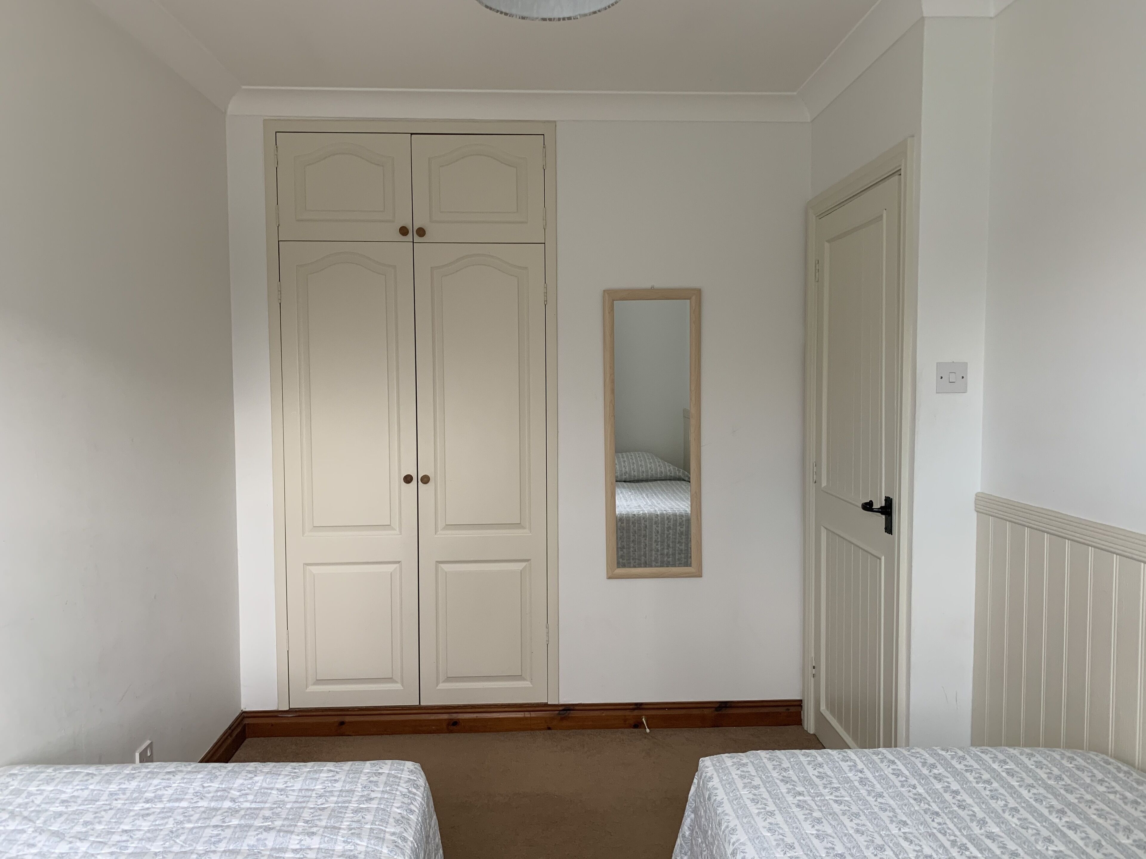 A bedroom with two beds, a wardrobe, and a mirror.