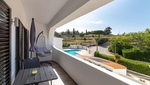 Een balkon met uitzicht op een zwembad, een hangstoel en een tafel met een glas.