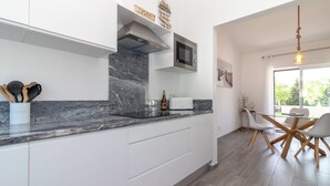 Een moderne keuken met witte kasten, een marmeren aanrechtblad en een ingebouwde magnetron.