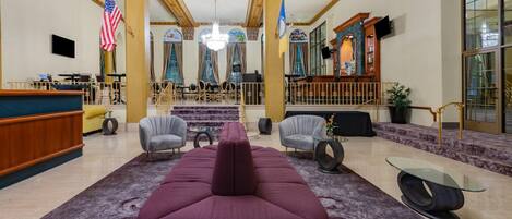 A lobby with a large purple sofa, a reception desk, and a staircase leading to upper floors.