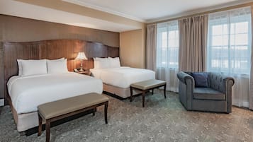 A hotel room with two beds, a sofa, a bench, a nightstand, and a lamp.