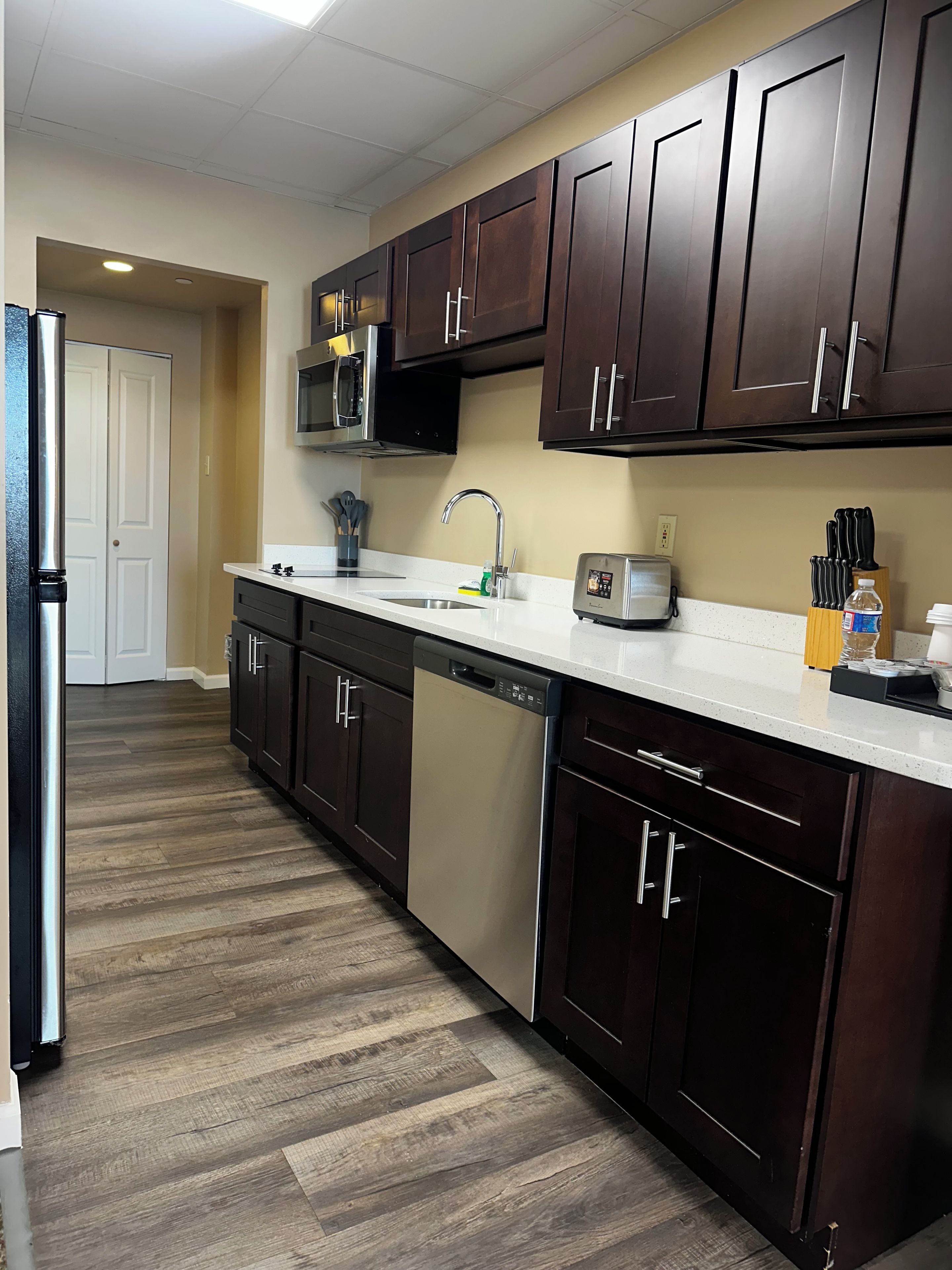 Una cocina con armarios de madera oscura, un refrigerador de acero inoxidable, lavavajillas, microondas y tostadora.