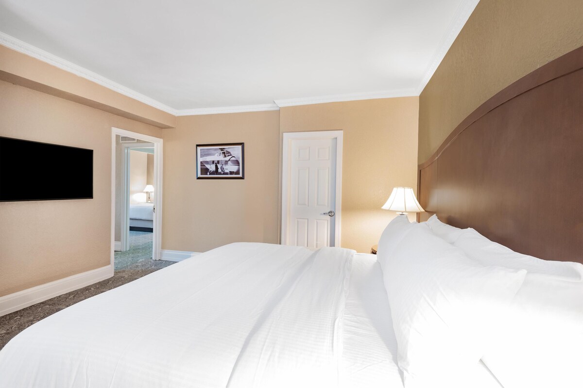 A hotel room with a large bed, a flat-screen TV mounted on the wall, a door, and a framed picture on the wall.