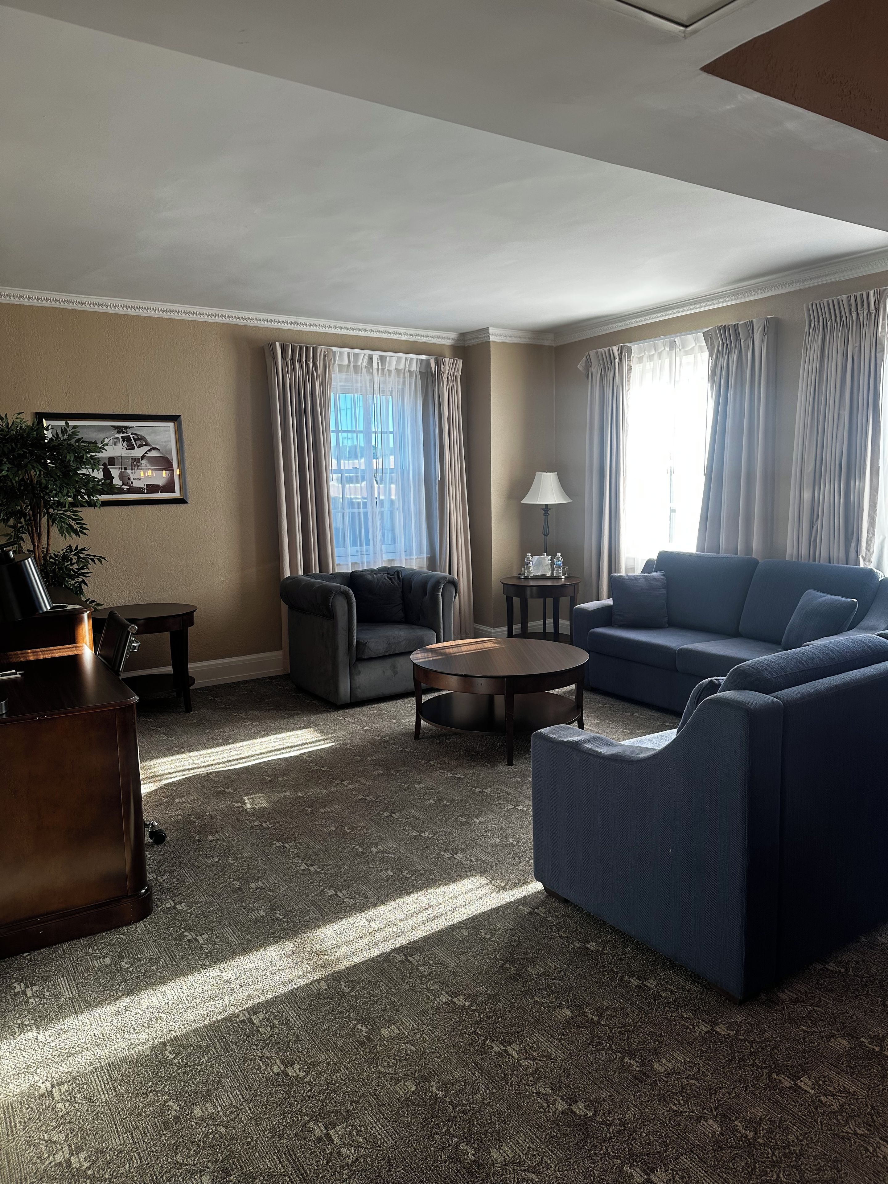 A living room with a sofa, armchair, coffee table, and a desk with a lamp.