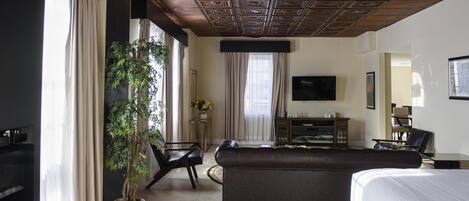A hotel room with a large bed, a sofa, a TV, a desk, and a potted plant.