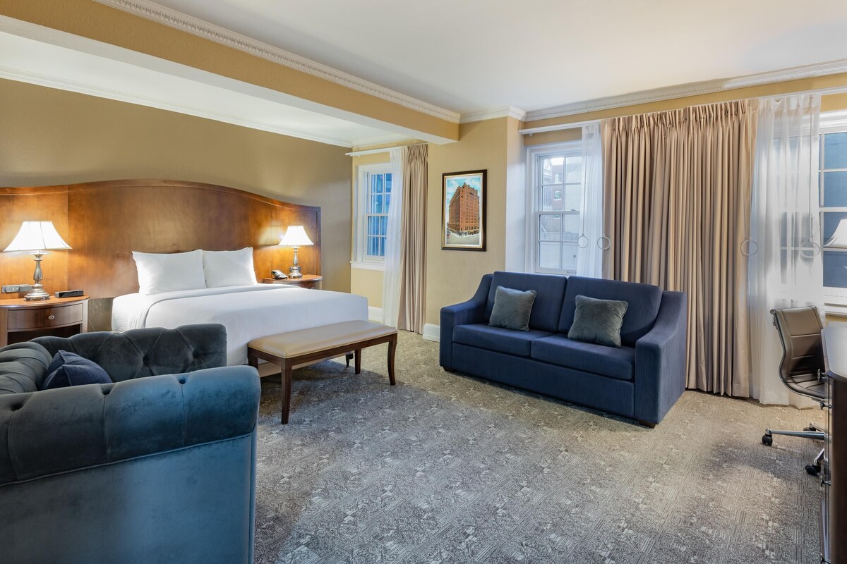 Une chambre d’hôtel avec un lit, deux tables de chevet avec des lampes, un canapé bleu, une petite table et une chaise.