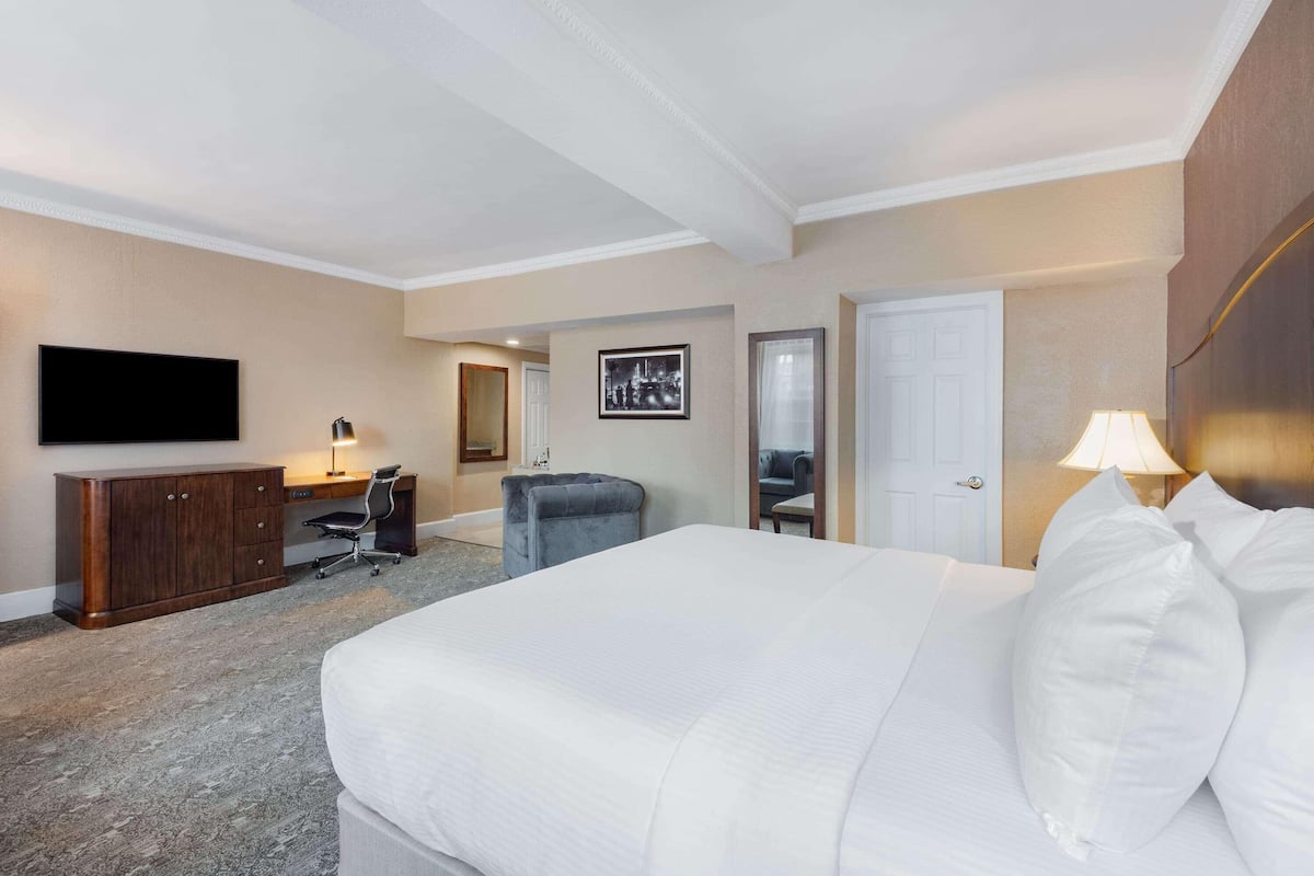 A hotel room with a large bed, a desk with a chair, a television, and a door.