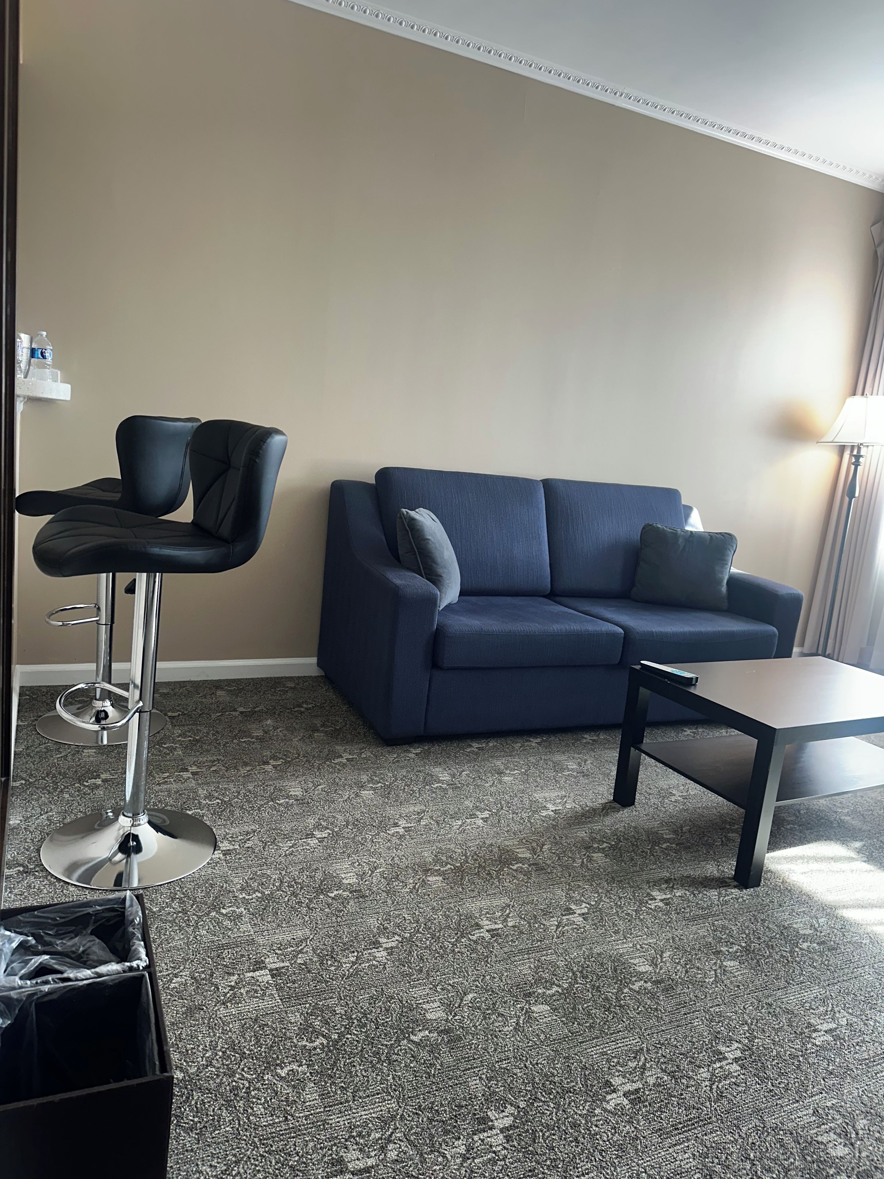 A living room with a blue sofa, a small table, and a bar stool.
