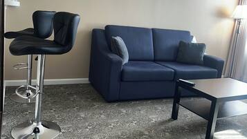 A living room with a blue sofa, a small table, and a bar stool.