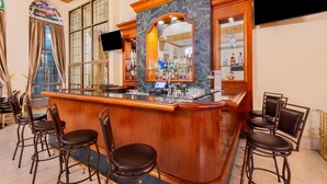 Una zona de bar con encimera de mármol, taburetes de madera y un salpicadero espejado.