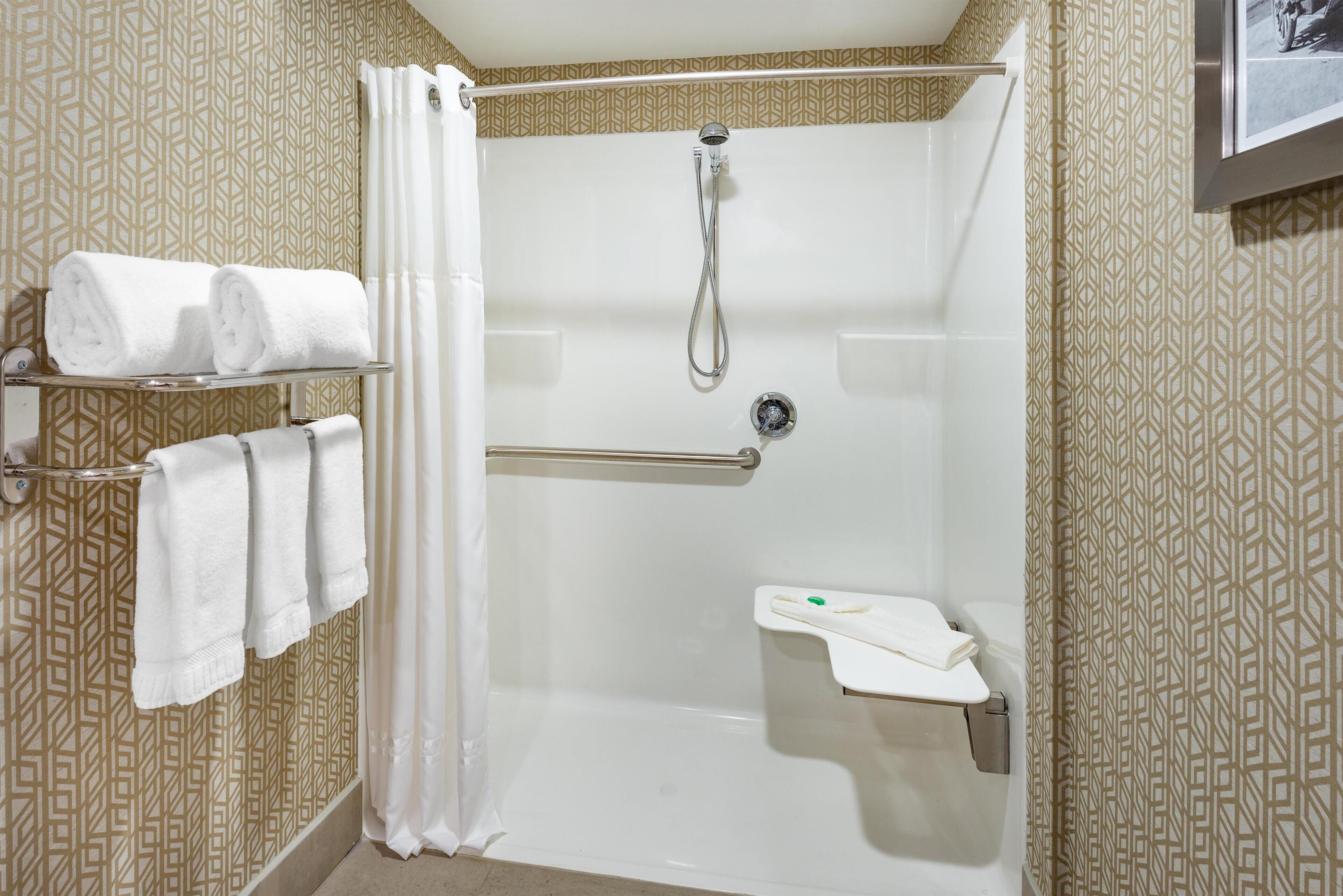 A shower area with a handrail, a showerhead, and a towel rack with towels.