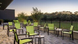 Ein Terrassenbereich im Freien mit grünen Stühlen und Tischen, umgeben von einem Zaun und Bäumen.