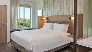 Une chambre d’hôtel moderne avec un grand lit, une tête de lit en bois et une vue sur les arbres par la fenêtre.