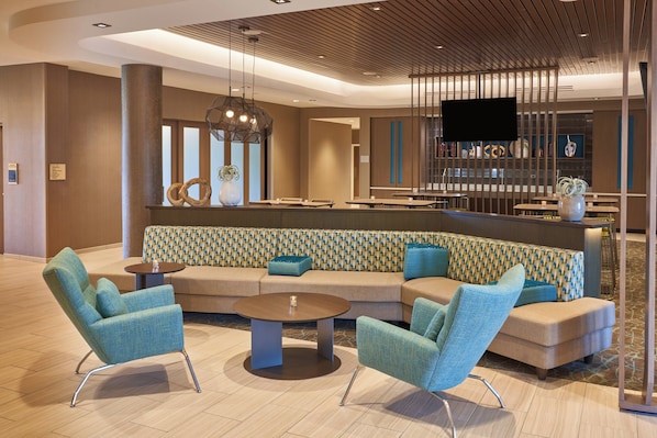 A modern lobby with a seating area, a bar, and a television screen.