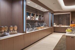 Una cucina d'hotel moderna con area buffet, inclusi distributori automatici di cibo e un'esposizione di frutta.