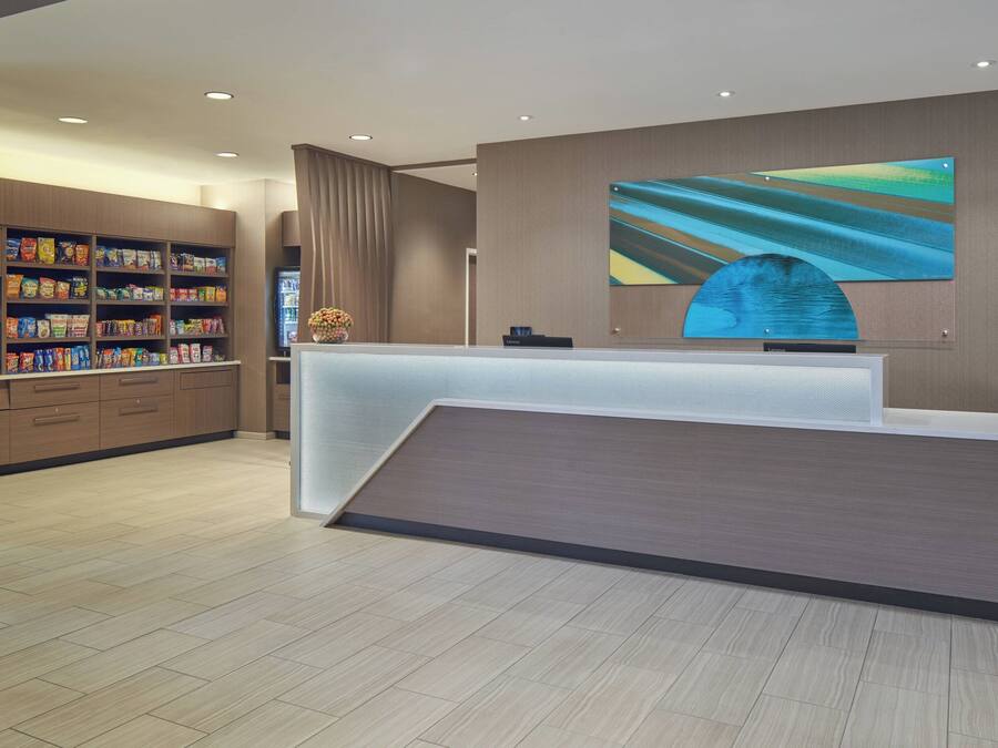 A modern reception area with a wooden reception desk, a large abstract painting, and a variety of snacks on shelves.