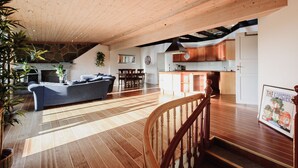 A spacious living area with a wooden ceiling, a sofa, a dining table, and a kitchen in the background. - Penthouse Apartment (Bergen)