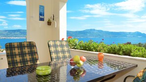 Un tavolo con vista sul mare e sulle montagne, due poltrone a quadri, una ciotola verde e un vaso con fiori.