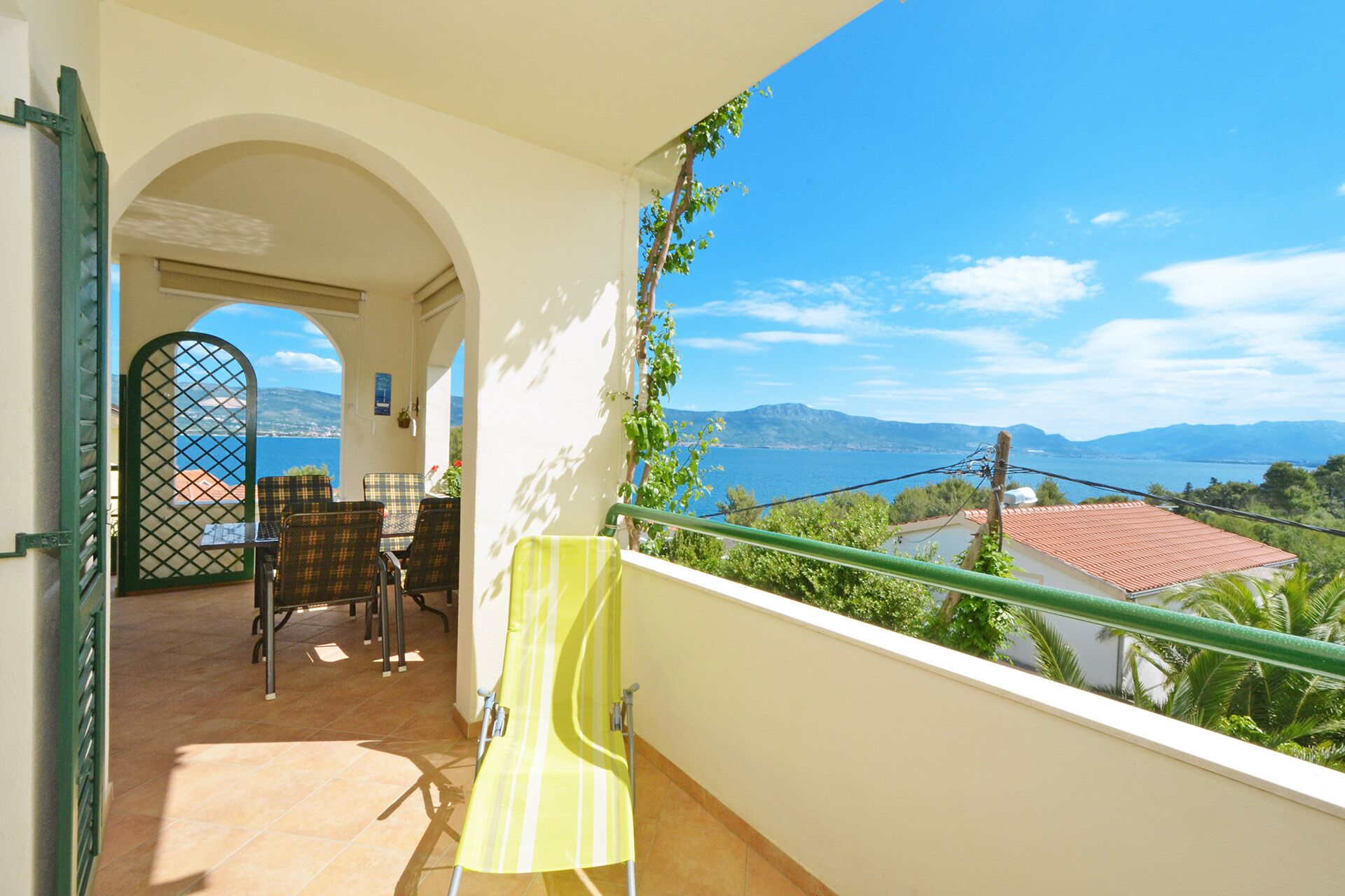 A balcony with a view of a coastal landscape, a table with chairs, and a yellow chair.