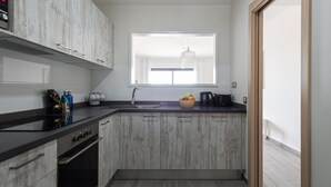 A modern kitchen with grey cabinetry, a black countertop, a built-in oven, and a window above the sink. - Apartamento con Terraza y piscina Pueblo Majorero (Caleta de Fuste - Antigua)