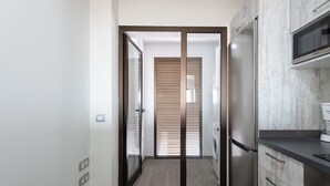 A modern kitchen with a stainless steel refrigerator, microwave, and oven. There is a sliding door leading to a laundry area with a washing machine. - Apartamento con Terraza y piscina Pueblo Majorero (Caleta de Fuste - Antigua)