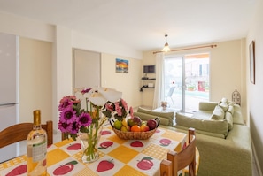 A dining area with a table set for two, a bottle of wine, and a fruit basket.