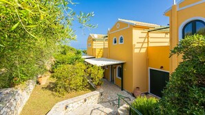 A yellow villa with a stone pathway, a covered patio, and lush greenery.
