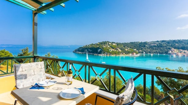 A table set for dining with a clear view of the sea and a sailboat in the distance.