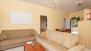 Ein Wohnzimmer mit zwei Sofas, einem Holztisch und einer Deckenleuchte. Durch einen offenen Durchgang ist ein Essbereich mit Tisch und Stühlen erkennbar.