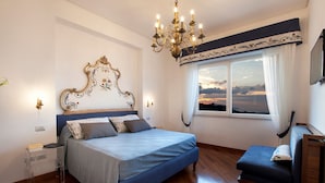 A bedroom with a large bed, a nightstand, a dresser, a window with curtains, and a chandelier.
