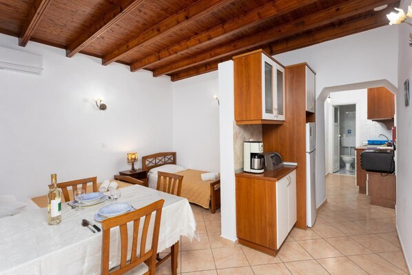 Een kleine kamer met een eettafel, stoelen, een bed, een kitchenette en een badkamer die door een open deur zichtbaar is.