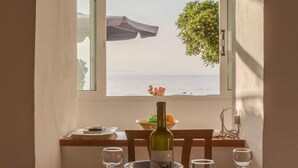 Une table à manger avec une bouteille de vin, des verres et une vue sur la mer par la fenêtre.