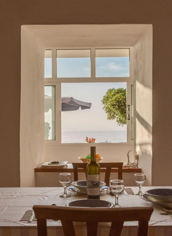 Une table à manger avec une bouteille de vin, des verres et une vue sur la mer par la fenêtre.