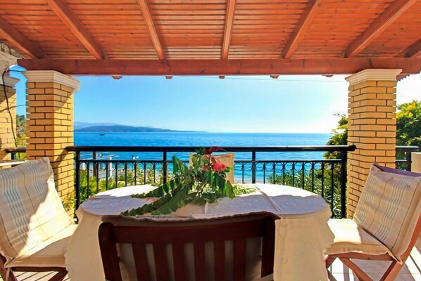 A covered outdoor seating area with a table and chairs, overlooking a body of water.