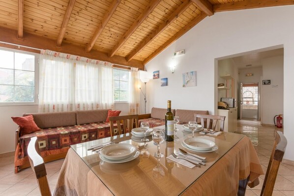 Un comedor con una mesa de madera dispuesta para cuatro, un sofá con un estampado y una botella de vino.