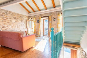 A bedroom with a stone wall, wooden beams, a pink sofa, and a staircase with teal railings.