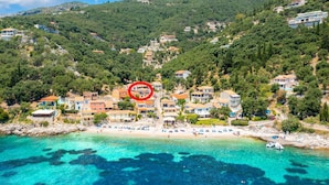 Un pueblo costero con casas en una colina, una playa con tumbonas y aguas turquesas cristalinas.
