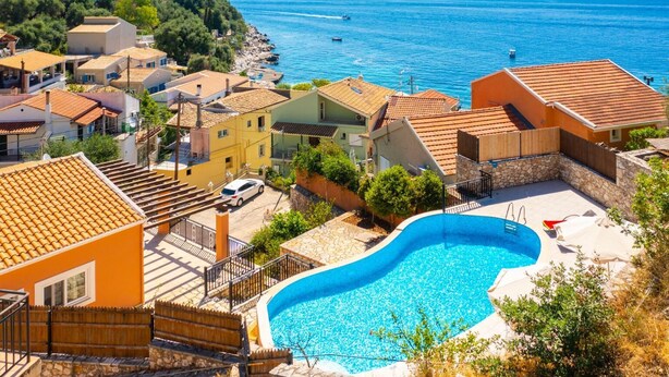 Zona residencial con piscina, casas con techos de tejas rojas y vista al mar.