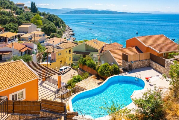 Un quartier résidentiel doté d’une piscine, de maisons aux toits recouverts de tuiles rouges et offrant une vue sur la mer.
