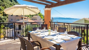 Una terraza con mesa lista para comer, con vistas panorámicas al mar y las colinas.