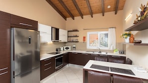 Una cocina moderna con refrigerador, horno, microondas y pileta integrados. Se observa una ventana con vista a un paisaje nevado, y el techo presenta vigas de madera a la vista.