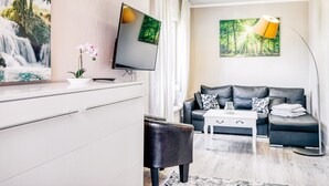 A modern living room with a flat-screen TV, a sofa, a coffee table, and a lamp. - Vacation apartment Waldesruh (Thale)